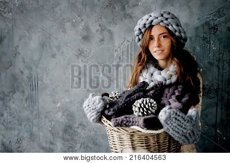 Winter fashion accessories.Young woman dressed for cold weather in grey snood hat and mittens holding a basket full of knitted clothes.