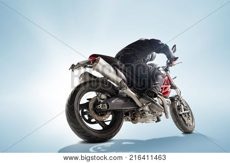 Biker in black jacket and helmet sitting on his sportive bike on blue studio background