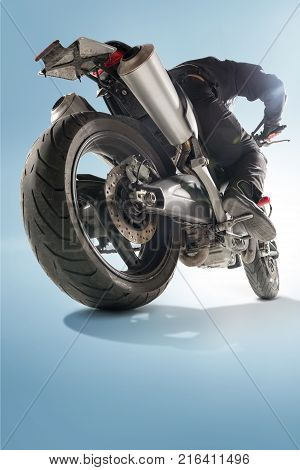 Biker in black jacket and helmet sitting on his sportive bike on blue studio background