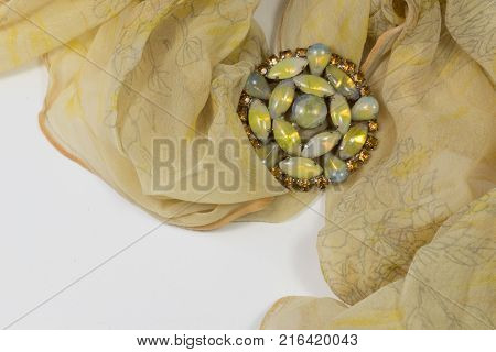 Swirling sheer yellow scarf with rhinestones and cabochons brooch on white horizontal aspect