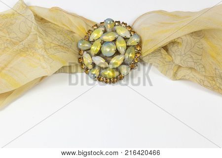 Swirling sheer yellow scarf with rhinestones and cabochons brooch on white horizontal aspect