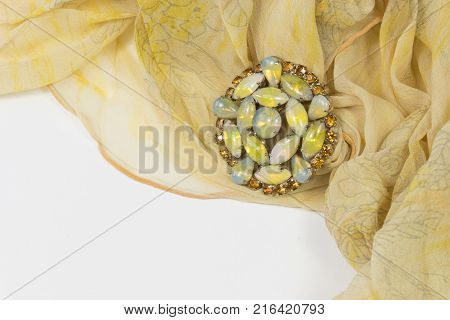 Swirling sheer yellow scarf with rhinestones and cabochons brooch on white horizontal aspect