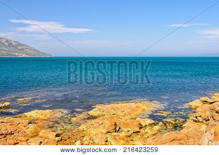 Blue water and rocks coloured by red lichen in the Freycinet National Park - Coles Bay, Tasmania, Australia
