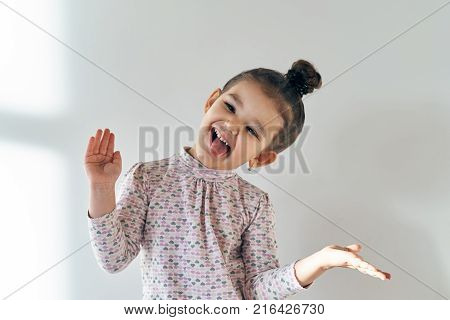 a little girl with a cheerful mischievous joyful expression of the Hamming and showing tongue at the camera waving. close-up portrait in natural light