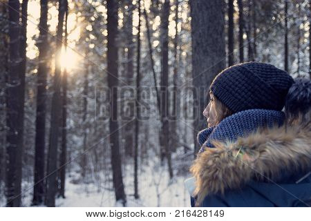 girl in a down jacket beanie in the winter woods at dawn
