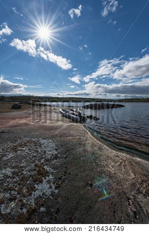 Empty white inflatable boat in direct sun on the colorful rocks of the lake shore. Sun flare or boche effects in the sky and on the rock in the right lower corner of the photo.