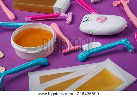 A close-up of a female epilator, disposable razor, wax strips, wax, wax in a cassette, are scattered and lie on a bright pink background.