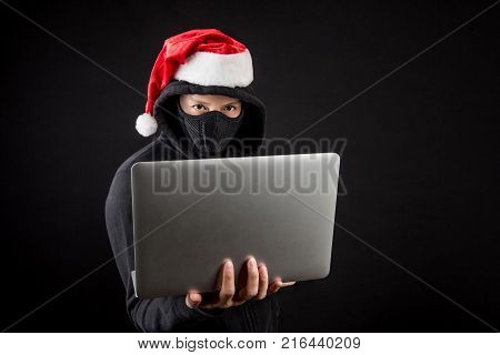 Mysterious male santa hacker holding laptop computer anonymous man on black background ransomware cyber attack and internet security on Christmas holiday concepts
