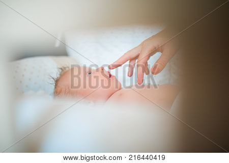 Mother playing with her baby, who lies on his back in the crib