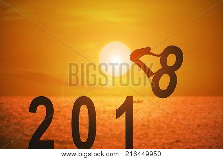 Silhouette of young man jumping over the numbers 2018 years with beautiful sunset at the sea concepts of news year and business target.