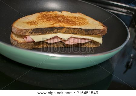 A grilled ham and cheese sandwich being cooked in a frying pan to a golden brown color.