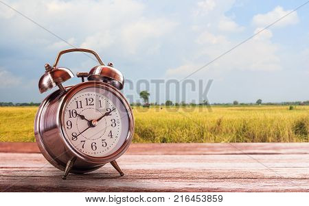 Retro alarm clock on a wooden table with blurred sky background. Photo in retro color image style. Top view with copy space for use.