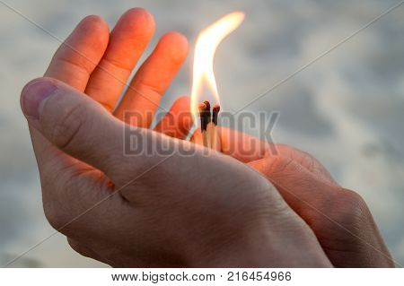 Burning matches in hands. The flame from the matches pointing to the up and left. Adult man sand background.