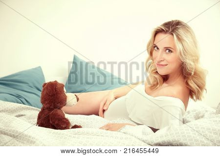 Pregnant young beauty awaiting her newborn while relaxing in bed