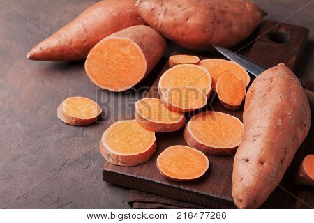 Organic sweet potatoes whole and sliced on wooden kitchen board.