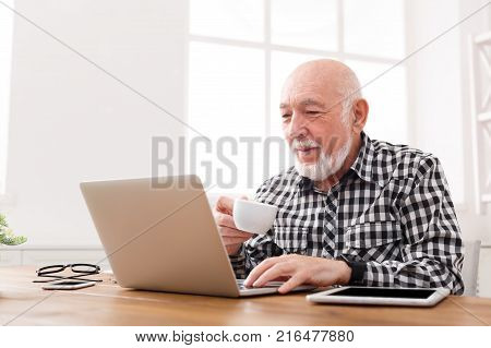 Mature man using laptop and writing in notepad at home desk. Education, recipe concept, copy space
