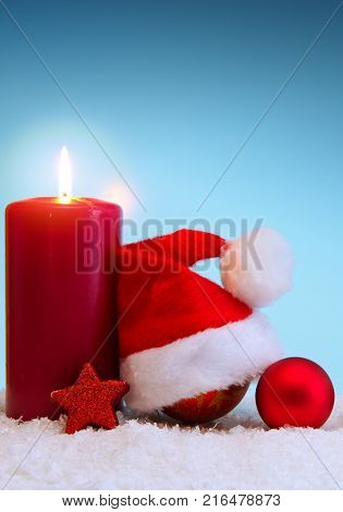 Avent candle and christmas decoration isolated on blue background. Christmas background with snow, candle and Santa Claus hat.
