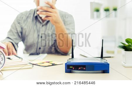 closeup of a wireless router and a man using smartphone on living room at home ofiice