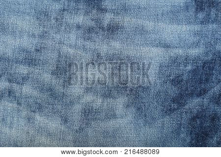 Dark indigo blue cotton jeans denim texture background with light washed distressed faded area, close up