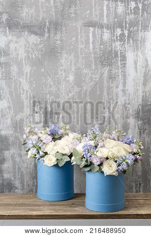 two flower bouquet in a hat box blue. standing on a wooden table. On the background old gray wall art. copy space. blue and white color