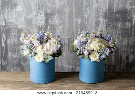 two flower bouquet in a hat box blue. standing on a wooden table. On the background old gray wall art. copy space. blue and white color