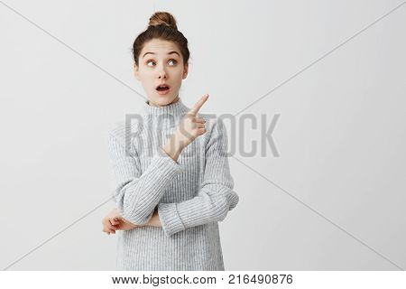 Teenage girl with wonder looking to side and showing with index finger. Curious female employee trying to pay attention over white background. Attention concept