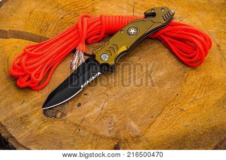 Pocket knife and paracord. Natural wood background.