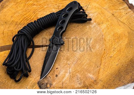 Black pocket knife and black parachute cord. Top view.