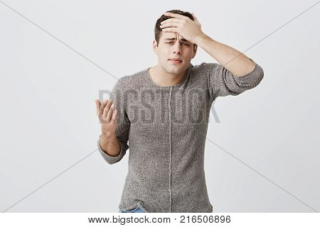 Tired dark-haired male student having headache after stress on exam. Hipster handsome man with sorrorful look holding his hand on head trying to find way out in difficult situation
