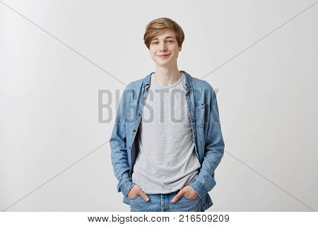 Smiling cheerful young European man expresses positive emotions as has good mood after walk with girlfriend. Pleasant looking fair haired guy smiles at good joke. Happiness and joy concept