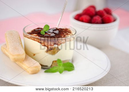 Tiramisu traditional italian dessert in a glass on white plate with ruspberries on the background.