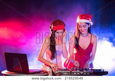 Portrait of active pretty young DJ woman playing music on laser lighting background.