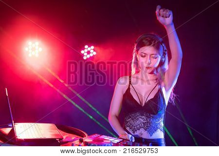 Portrait of active pretty young DJ woman playing music on laser lighting background.