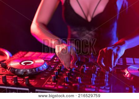 Portrait of active pretty young DJ woman playing music on laser lighting background.