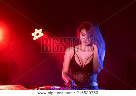 Portrait of active pretty young DJ woman playing music on laser lighting background.