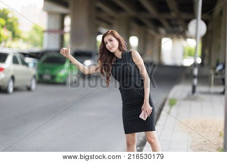 Young Beautiful Asian Straight Hair Woman Asking for a Taxi Raising her Arms . Transport in The City Concept