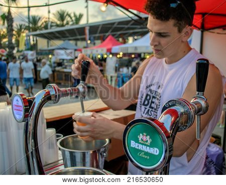 Netanya, Israel - July 13 2017: Young man-customer pours large beer in plastic cup at beer festival. City summer event.