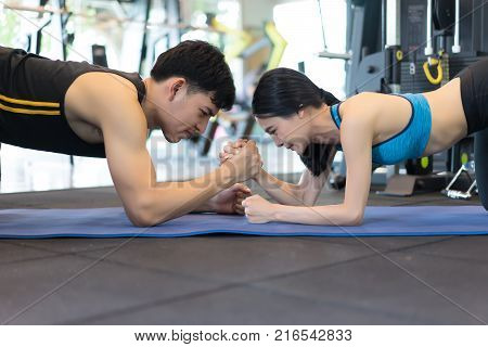 Sporty couple doing push ups plank and arms wrestling exercise on mat in gym