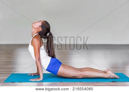 Yoga girl doing cobra backbend pose during yoga practice at fitness studio. Asian woman practicing on exercise mat.