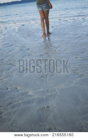 Legs with Footprints on Sand and a girl walking ahead