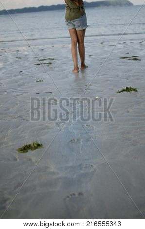Legs with Footprints on Sand and a girl walking.