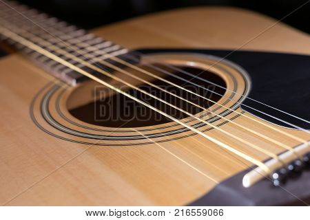 Close-up of rosette and strings of the acoustic guitar on black background.