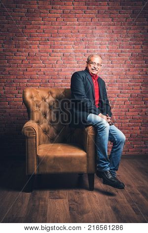 stylish senior indian man in suit sitting on sofa or wing chair. Portrait of Indian or asian millionaire or rich man
