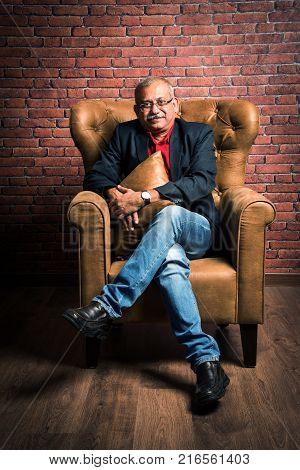 stylish senior indian man in suit sitting on sofa or wing chair. Portrait of Indian or asian millionaire or rich man