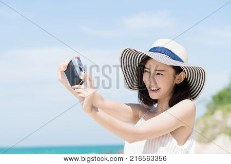 Young asian woman selfie by camera on the beach with sunny day. Happy girl selfie and smile with blue sky. Travel and lifestyle summer concept.