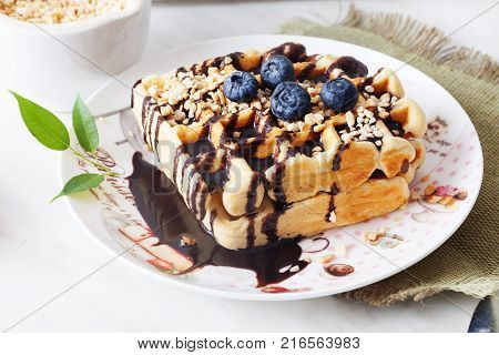 Belgian waffles with peanut chocolate sauce and blueberry, bilberry, whortleberry, huckleberry, hurtleberry, blaeberry on a plate in still life straw