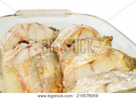 Fragment of the rectangular glass casserole pan with several baked pieces of the red cod closeup on a white backgroundr