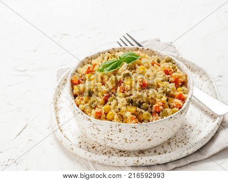 Close up view of cauliflower rice with vegetables. Organic paleo Cauliflower Rice with corn, green peas and carrots on white concrete background. Copy space.