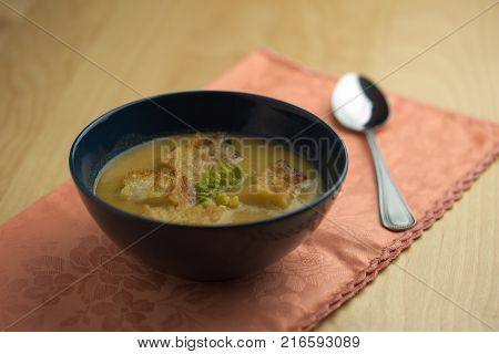 Cauliflower soup into cup, croutons of bread over tablecloth with spoon