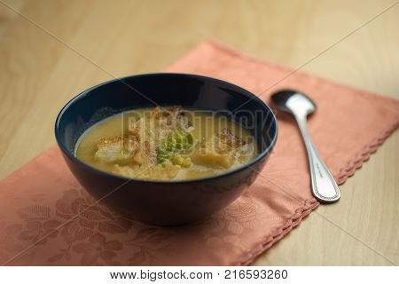 Cauliflower soup into cup, croutons of bread over tablecloth with spoon